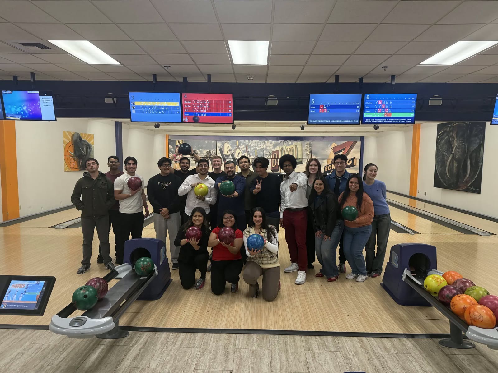 A large group of members holding bowling balls and posing together at a bowling alley